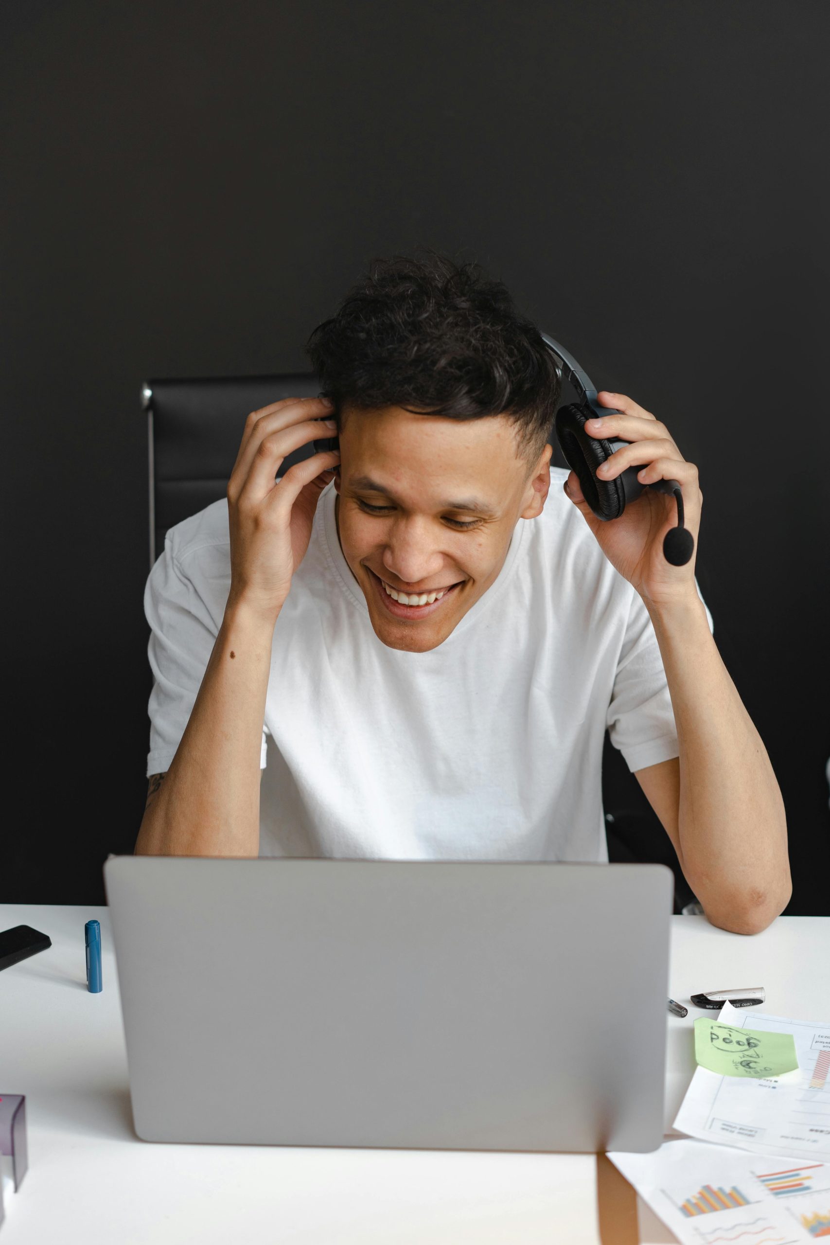 Cheerful customer service agent smiling while using laptop with headset in a modern office.